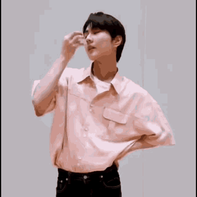 a man in a pink shirt and black jeans is standing with his hands on his hips .