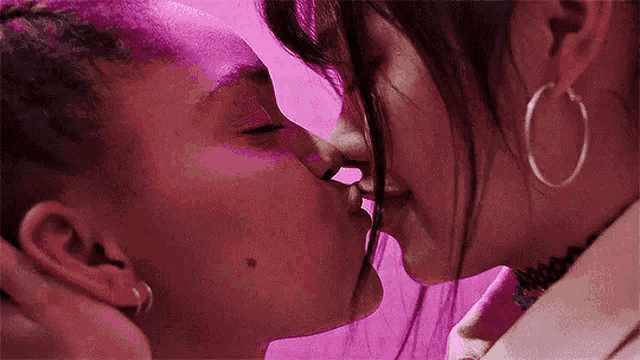 a couple of women are kissing each other on the cheek in front of a pink background .