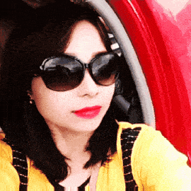 a woman wearing sunglasses and a yellow shirt takes a selfie