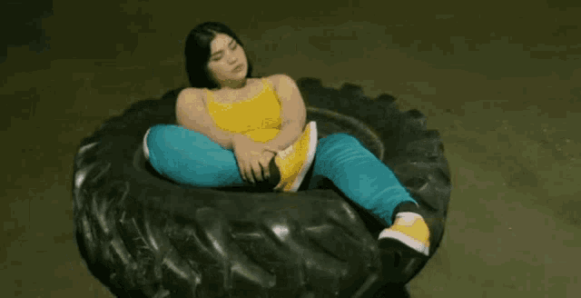 a woman in a yellow tank top and blue pants is laying on a large tire