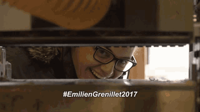 a woman wearing glasses is smiling while looking through a window with the words #emiliengrenillet2017 written below her