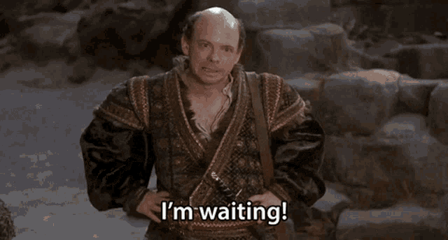 a bald man says " i 'm waiting " in front of some rocks