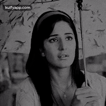 a black and white photo of a woman holding an umbrella and looking at the camera .