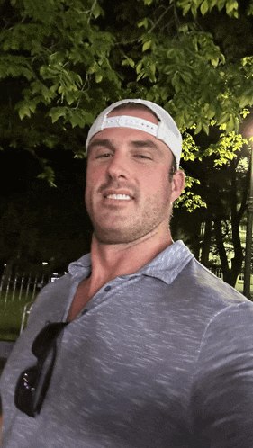 a man wearing a grey shirt and a white hat is smiling for a photo