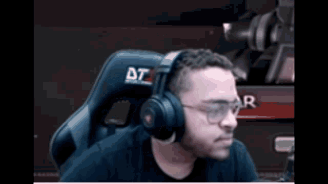 a man wearing headphones and glasses is sitting in a chair with a dt logo on it .