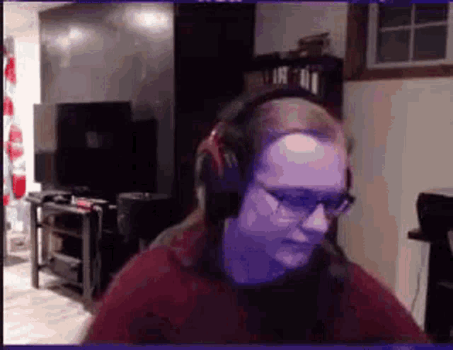 a man wearing headphones and glasses is sitting in front of a tv .