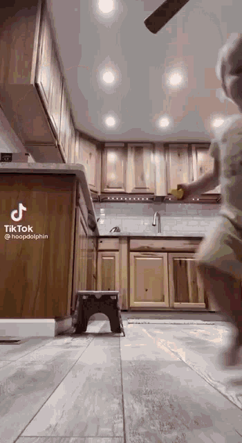 a little girl is standing in a kitchen with wooden cabinets and a step stool .