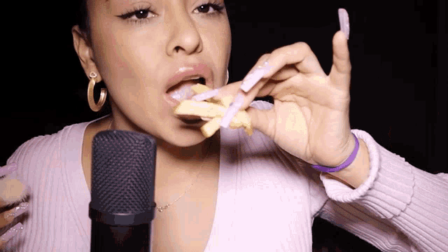a woman with long nails is eating french fries in front of a black microphone