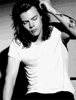 a black and white photo of a man with long hair wearing a white shirt and a tattoo on his arm .