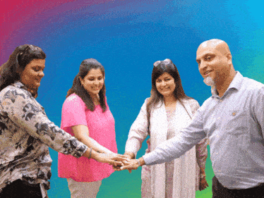 a group of people are putting their hands together in front of a colorful background