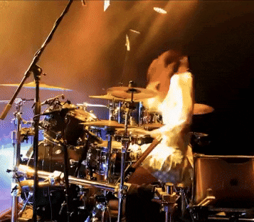 a person is playing drums on a stage with a microphone in the background