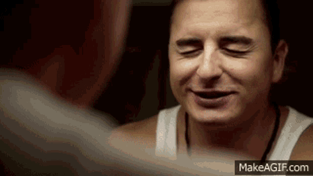 a man in a white tank top is looking at himself in a mirror with his eyes closed