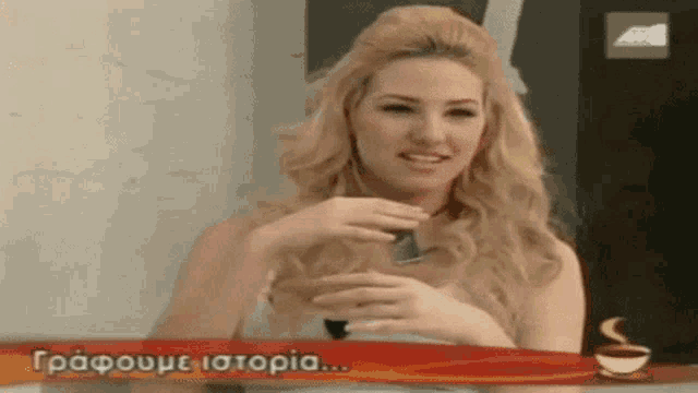 a woman is sitting at a table with a cup of coffee and a sign that says " graphome istoria "