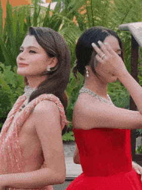 two women are standing next to each other one is wearing a red dress and the other is wearing a pink dress