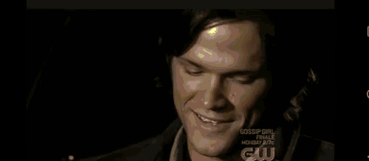 two men are sitting next to each other in a dark room and the words gossip girl are on the bottom of the screen .