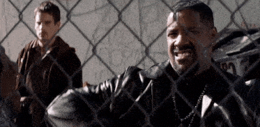 a man in a leather jacket is behind a chain link fence with another man behind him