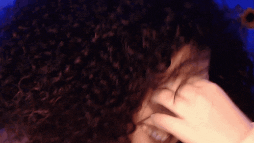 a woman with curly hair is covering her eyes with her hand