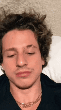 a close up of a man laying on a bed with his eyes closed and a necklace around his neck .