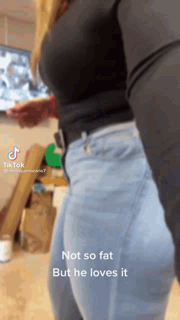 a woman wearing a black shirt and blue jeans is standing in front of a tv .