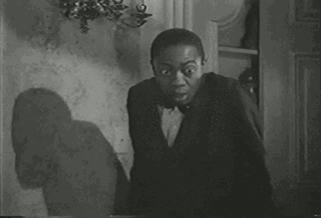 a black and white photo of a man in a suit and bow tie making a surprised face .