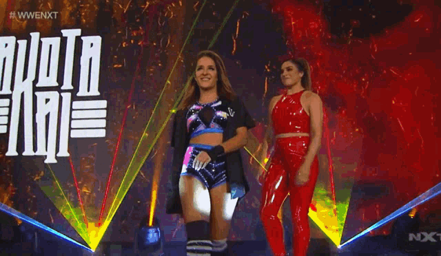 two women are walking on a stage in front of a sign that says next