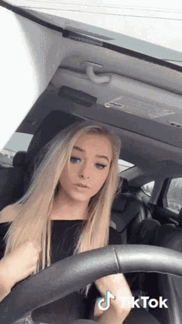 a woman is sitting in the driver 's seat of a car with a tiktok sticker on her face .