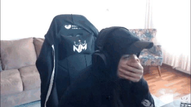 a person covering their mouth with their hands while wearing a nm hat
