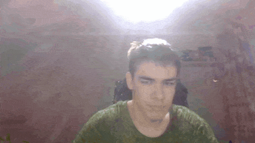a man in a green shirt is looking at the camera while sitting in a chair .