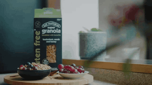 a box of super granola sits next to a bowl of grapes