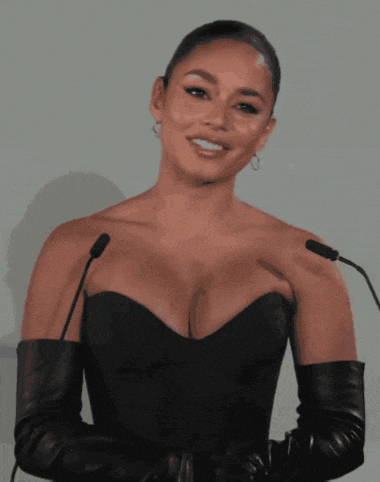 a woman in a black dress and leather gloves stands in front of two microphones