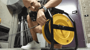 a man with a watch on his wrist is kneeling down next to a yellow cable reel