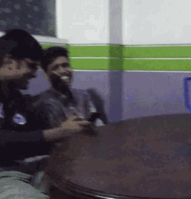 two men are sitting at a table and one is using a phone