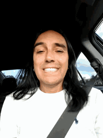 a man with long hair wearing a seat belt smiles