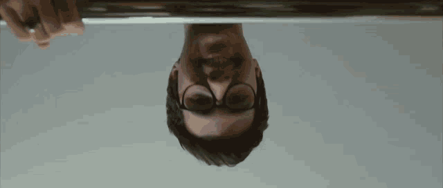 a man wearing glasses is upside down and looking down