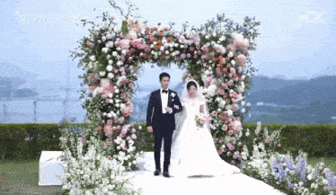 a bride and groom are walking under a floral archway