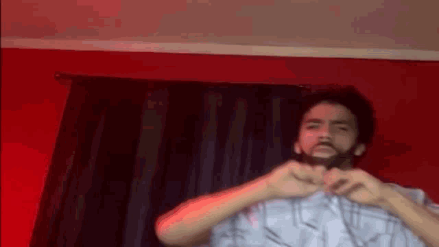 a man with a beard is making a heart shape with his hands in front of a red curtain .