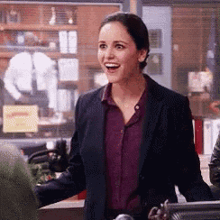 a woman in a suit and a purple shirt is smiling while standing in a room .