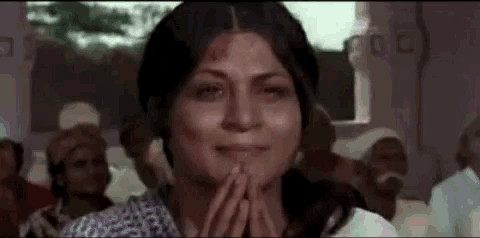 a woman is smiling with her hands folded in front of her face in a crowd of people .