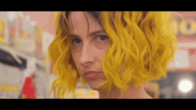 a close up of a woman 's face with yellow hair looking at the camera .
