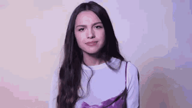 a young woman with long hair is wearing a white shirt and a purple dress and making a funny face .