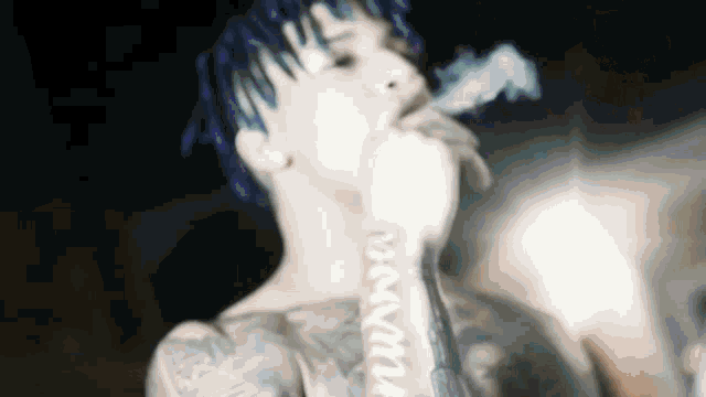 a man with blue hair and tattoos is smoking a cigarette .