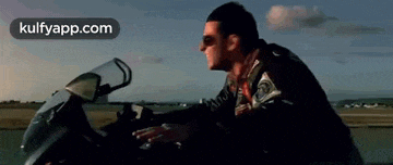 a man in a leather jacket is riding a motorcycle on a runway .