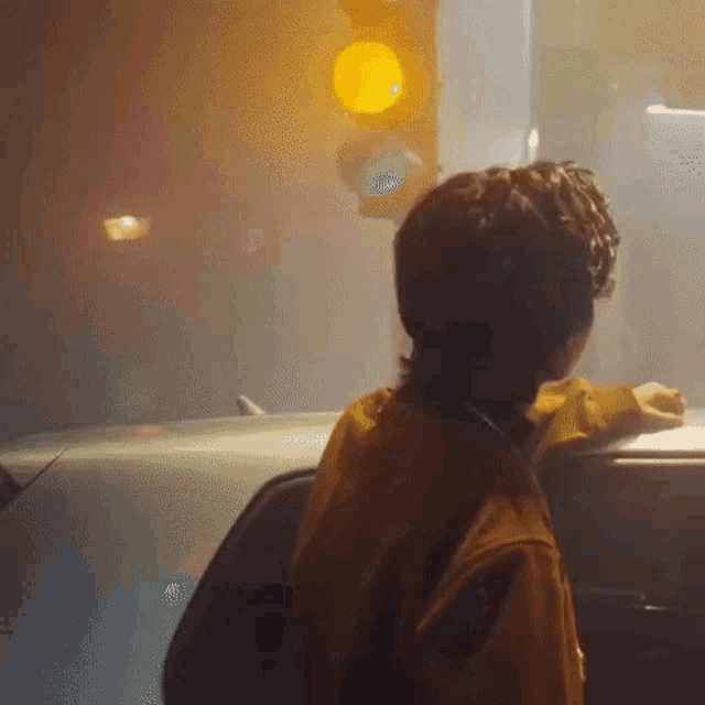 a man is leaning on the roof of a car at a traffic light .