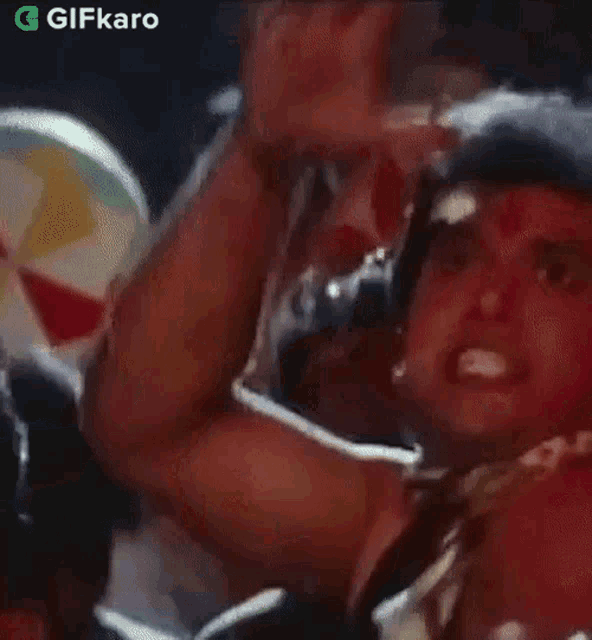 a man is screaming in a crowd of people while holding a cup and waving his hands in the air .