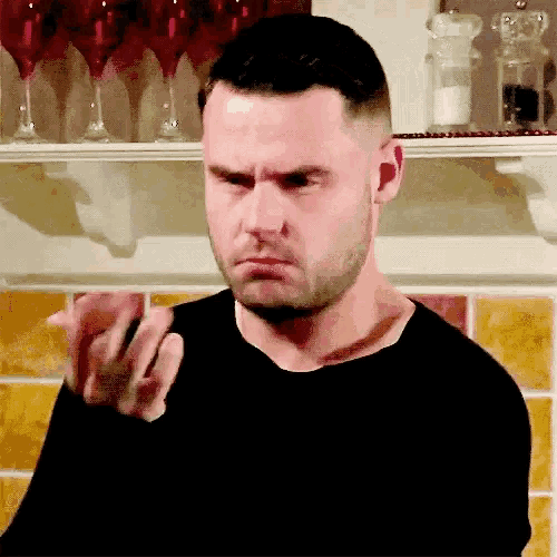 a man in a black shirt is making a funny face in front of a shelf with wine glasses on it