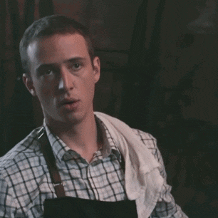 a man wearing an apron and a plaid shirt has a towel around his neck