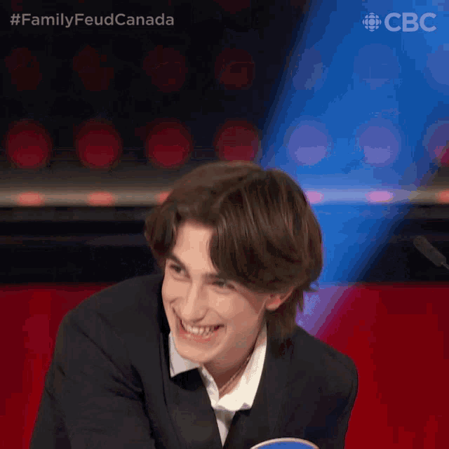 a young man in a suit and white shirt is smiling in front of a cbc logo