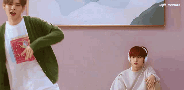 a man in a green cardigan is dancing while another man wearing headphones sits on a couch .
