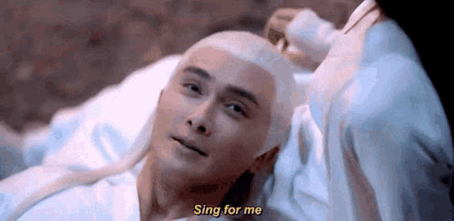 a man with white hair is laying on a bed with a woman holding his head .