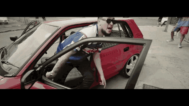 a man getting out of a red car wearing a shirt that says ' new york yankees ' on it